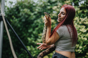 A smiling young girl interacts with a snake in an outdoor setting, illustrating a bond between humans and nature. The vibrant greenery enhances the scene's natural and adventurous feel.