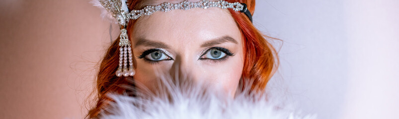 Portrait of a girl with make-up, whose face is covered with a feather fan. Eyes close up on banner
