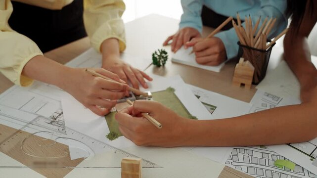 Smart architect and safety engineer discussion about building blueprint on table with architectural document, measurement tools and wooden block scatter around at modern office. Closeup. Delineation.