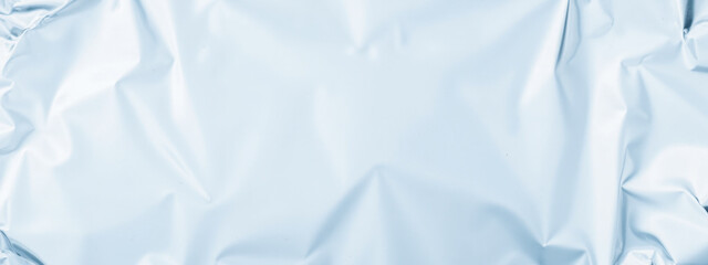 Obraz premium Crumpled light blue foil texture background, smooth metallic surface, soft reflective design, shiny wrinkled pattern, elegant material for modern creative visual