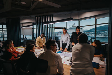 A diverse group of business colleagues engaged in an intensive brainstorming session, exchanging ideas and analyzing plans in a modern, well-lit office environment. Multicultural teamwork for