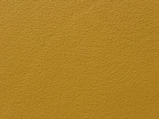 Close-up of a textured mustard yellow wall with a rough finish, offering a vibrant and minimalistic background. Perfect for use in design projects, advertising, or as a bold decorative element. 