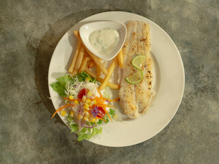 Fried fish fillet with french fries and salad on white plate