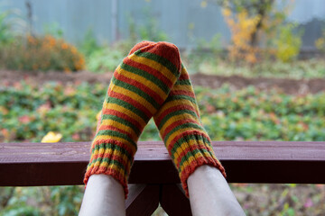 Male feet in striped socks, knitted from yarn in orange, yellow and green colors, on the railing of...
