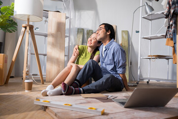 Asian couple sitting in renovated home, proudly reflecting on their accomplishments while planning...
