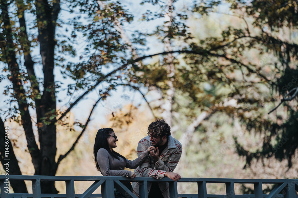 Wall mural A happy couple shares a playful moment on a bridge surrounded by vibrant forest foliage. They are smiling and enjoying the serene natural setting on a sunny day.