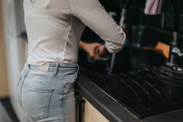 A woman is seen washing dishes at a kitchen sink, showcasing daily household chores and routine cleaning. She wears casual attire, emphasizing a home setting and the simplicity of domestic life.