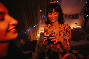 A young woman joyfully celebrating her birthday with a friend in a warmly decorated room. The festive atmosphere is highlighted by twinkling lights and colorful decorations, setting a cheerful mood.