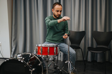 A musician focuses on tuning his drum set in a rehearsal studio. The scene highlights dedication and preparation in the music world, emphasizing attention to detail and commitment.