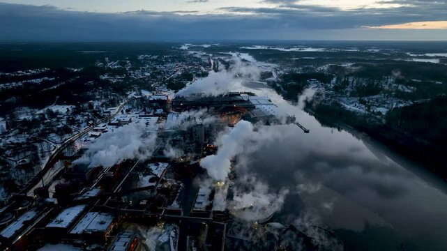 Aerial view of paper mill Industrial plant emitting smoke over river at sunset