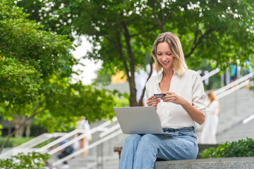 Caucasian Woman Using Laptop and Credit Card to Perform Online Transaction While Sitting Outdoor a Park