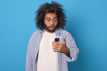 Man of Indian and Arabian descent gazes in astonishment at his phone. His curly hair and expressive...