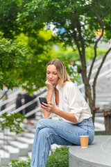 Obraz premium Caucasian Woman Sitting and Using Phone While Having a Cup of Coffee Outdoor a Park