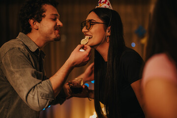 Group of friends joyfully celebrating a birthday at home, sharing laughter and snacks. A sense of warmth and friendship fills the festive atmosphere, creating memorable moments together.