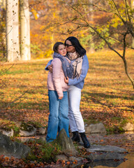 Fototapeta premium Happy single mom and her teenage daughter on walk in fall park. Mom lovingly hugs and kisses girl. Motherhood. Family Day. Time together. Active vacation in nature.