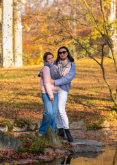 Fototapeta premium Happy single mom and her teenage daughter on walk in fall park. Mom lovingly hugs and kisses girl. Motherhood. Family Day. Time together. Active vacation in nature.