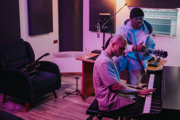 Two musicians work together in a studio setting, playing instruments and creating music. The ambient lighting and modern equipment contribute to an inspiring and creative atmosphere.