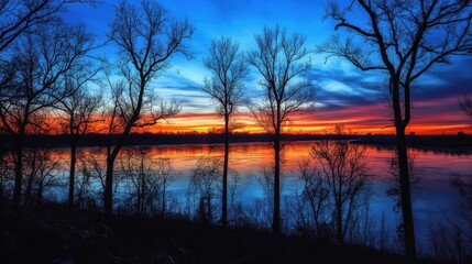 A breathtaking panorama of the sunrise illuminating the sky over the tranquil river at dawn with silhouettes of trees along the shore