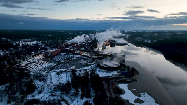 Smoke billowing from industrial paper mill chimneys by river in winter