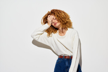 Woman with curly hair expressing frustration against a plain background She wears a white sweater...