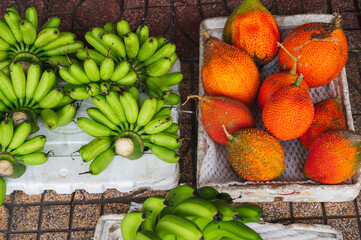 ripe orange Momordica Cochin fruit and green bananas at the local market