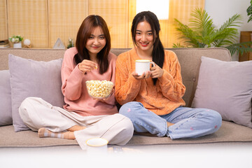 Wondered amazed impressed girl gesturing forefinger eating popcorn watching funny comic program with friend sitting in living room indoor enjoying interesting film