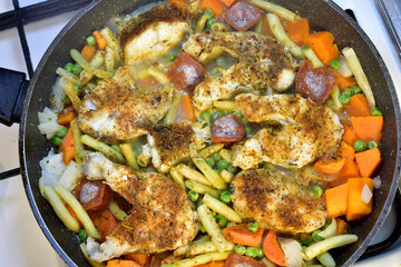 Cod fish with vegetables is cooked in a frying pan, top view.
