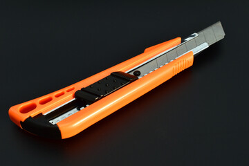 A construction knife with a retractable blade lies on a black background.