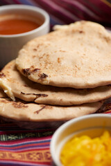 Pupusas with curtido and sauce served on a tamale leaf atop a wooden surface, highlighting traditional Central American flavors.