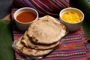 Pupusas with curtido and sauce served on a tamale leaf atop a wooden surface, highlighting traditional Central American flavors.