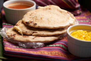 Pupusas with curtido and sauce served on a tamale leaf atop a wooden surface, highlighting traditional Central American flavors.