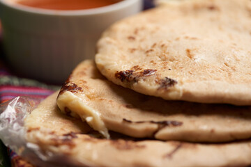 Pupusas with curtido and sauce served on a tamale leaf atop a wooden surface, highlighting traditional Central American flavors.