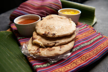 Pupusas with curtido and sauce served on a tamale leaf atop a wooden surface, highlighting traditional Central American flavors.