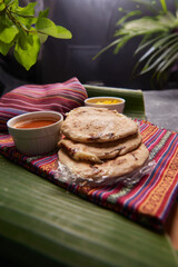 Pupusas with curtido and sauce served on a tamale leaf atop a wooden surface, highlighting traditional Central American flavors.