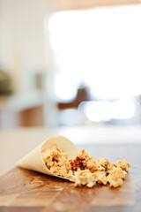Caramel popcorn spilling from paper cone onto wooden table.