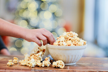 Hand reaching for popcorn in a bowl with festive bokeh lights.