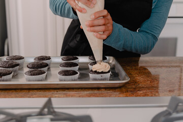 Baker adding frosting to chocolate cupcake sitting on tray