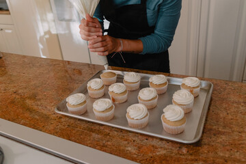 Baker using pastry bag to add frosting to vanilla cupcakes