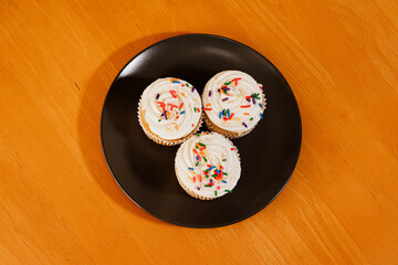 Trio of vanilla cupcakes with rainbow sprinkles sitting on black plate