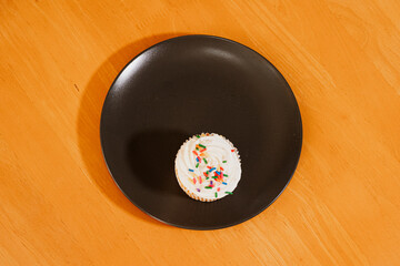 Vanilla cupcake sitting alone on black plate on wooden table