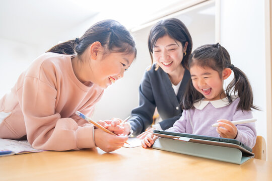 メインビジュアルにも！逆光の中、勉強や宿題をみるお母さんや塾の先生　小学生低学年の笑顔の子供「タブレットでも勉強楽しい」