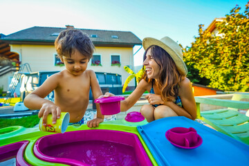 Mother and son playing with water table toys in backyard during summer vacation