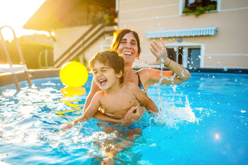 Mother and son laughing and splashing in swimming pool during summer vacation
