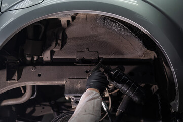 An auto mechanic applies anti-corrosion mastic to the underbody of a car.