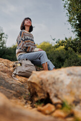 Naklejka premium Active lifestyle..A young woman in a stylish sweater enjoys a day in the mountains, sitting on the rocks.