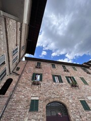 Rustic stone building with cloudy sky and green shutters. Assisi, Italy.