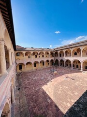 Fototapeta premium Historic courtyard with arches under a clear blue sky. Assisi, Italy.
