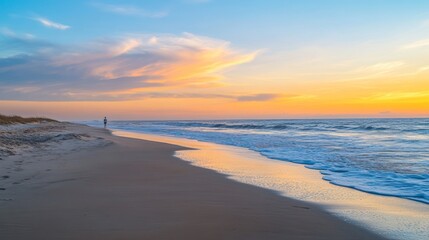 Obraz premium Solitary figure walking on a tranquil beach at sunrise, with soft pastel colors in the sky and gentle waves.