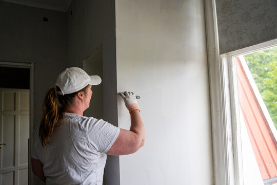 Rear view of female repairperson plastering wall at workplace