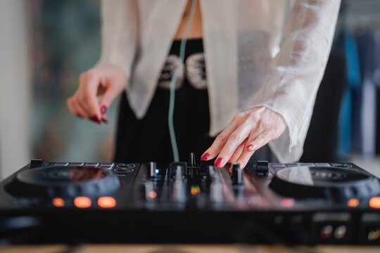 close-up shot of a woman’s hands with painted nails actively working on a DJ controller during a music mixing session in a modern, stylish home studio environment.
